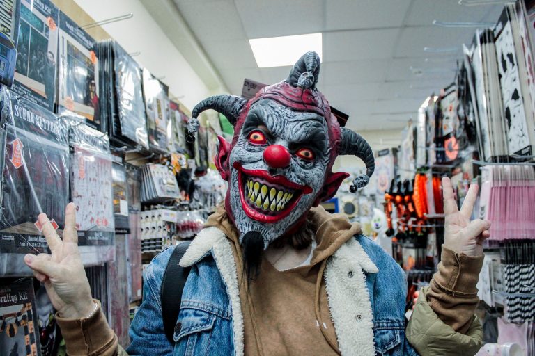A man in a denim jacket among the shelves of merchandise in the store donned a hell clown mask