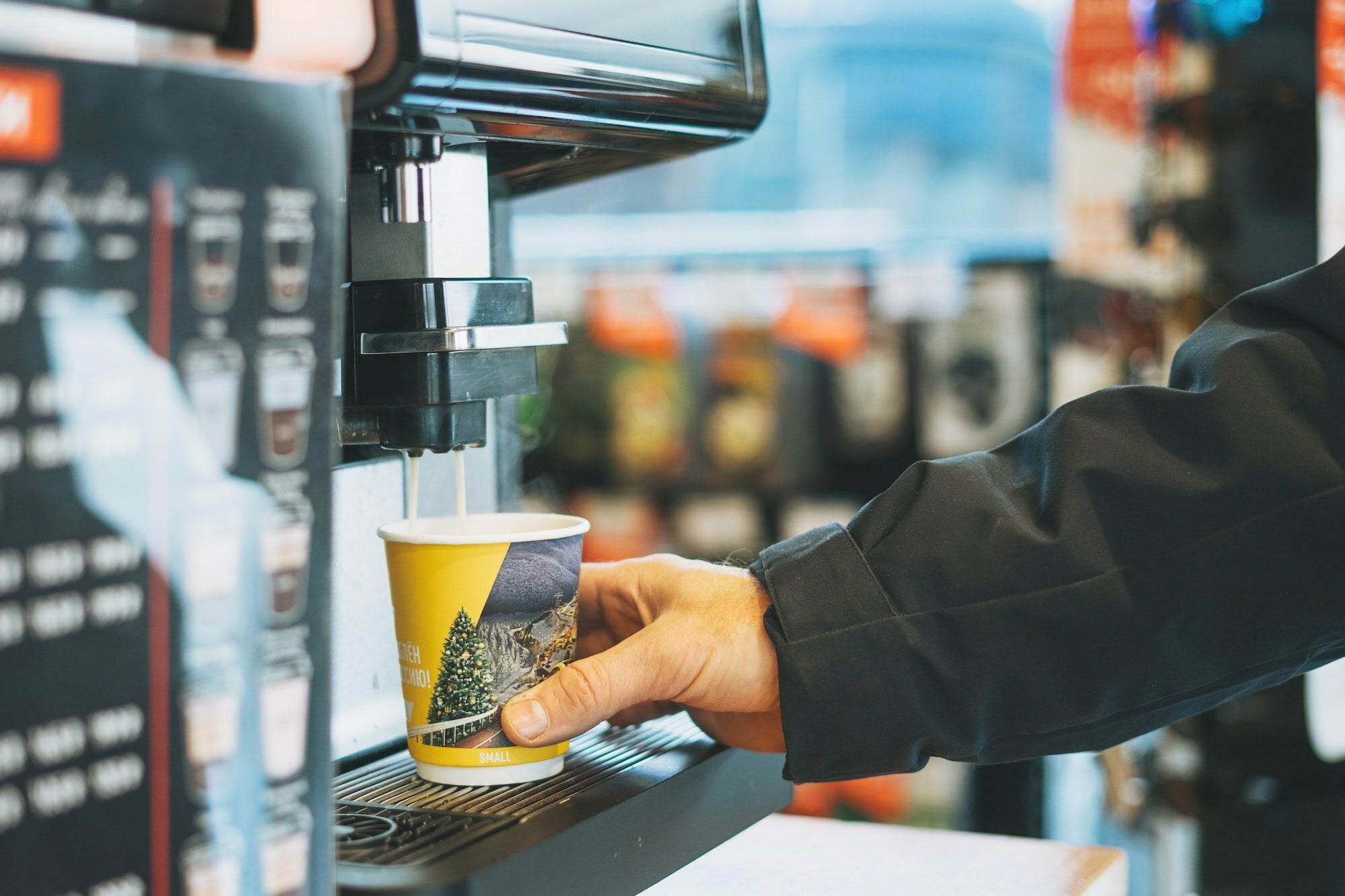 Young man driver pours coffee to go in the store at the gas station